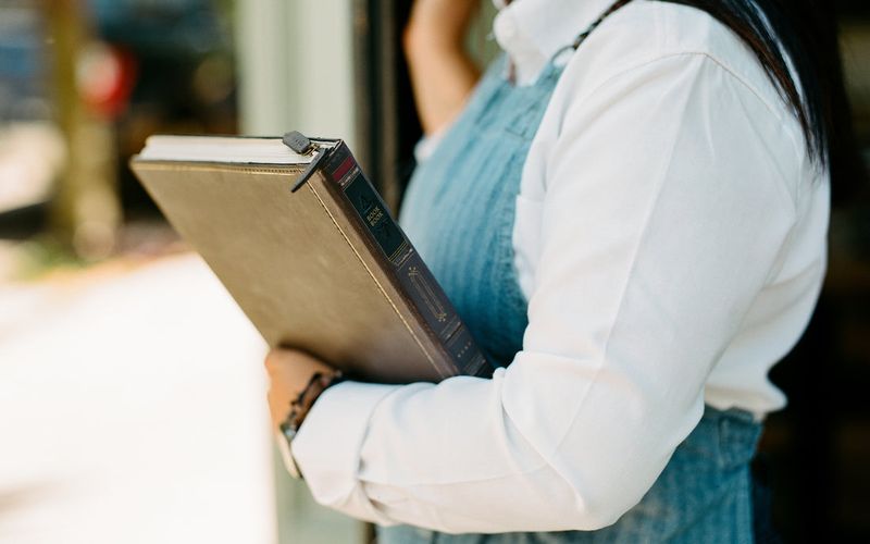 A woman is holding a closed BookBook case from Twelve South, designed for Apple