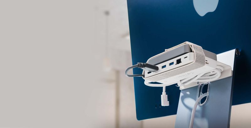 A promotional image from Twelve South showcasing its BackPack matte white aluminum shelf attached to the back of a blue 24-inch M1 iMac and housing an external hard drive