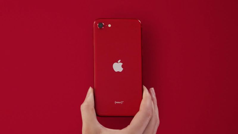 A hand showing holding a red iPhone SE 2, set against an all-red background