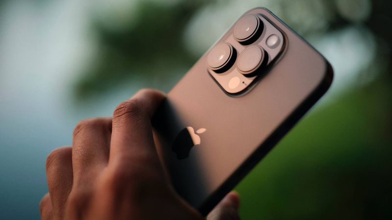 Male hand holding an iPhone 14 Pro Max above a river, taking a picture at sunset