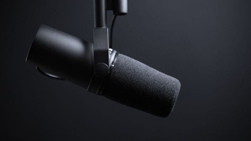 Closeup of a podcasting microphone suspended from above, set against a black gradient background