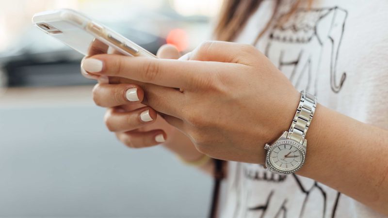 Young woman holding her gold iPhone XS in hands and typing on the touchscreen