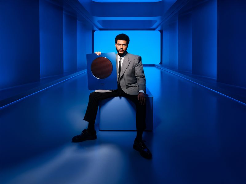 A photograph showing Canadian singer The Weekend sitting on a chair and holding his physical Apple Music Award