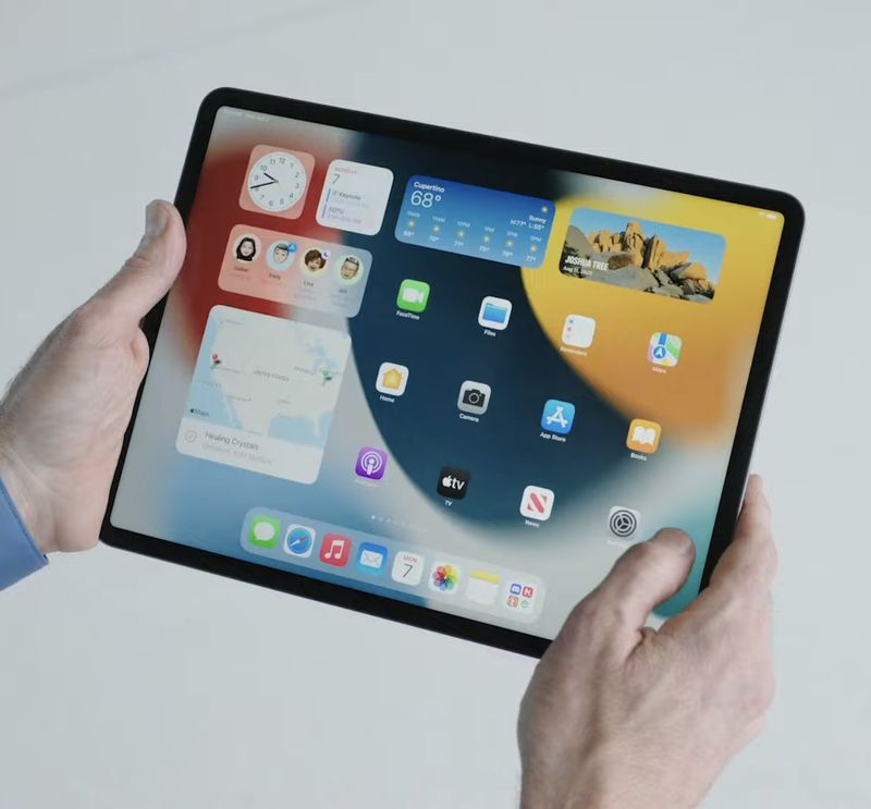 A photo showing an iPad Pro held in hands with the home screen shown with the Weather widget and other widgets and icons