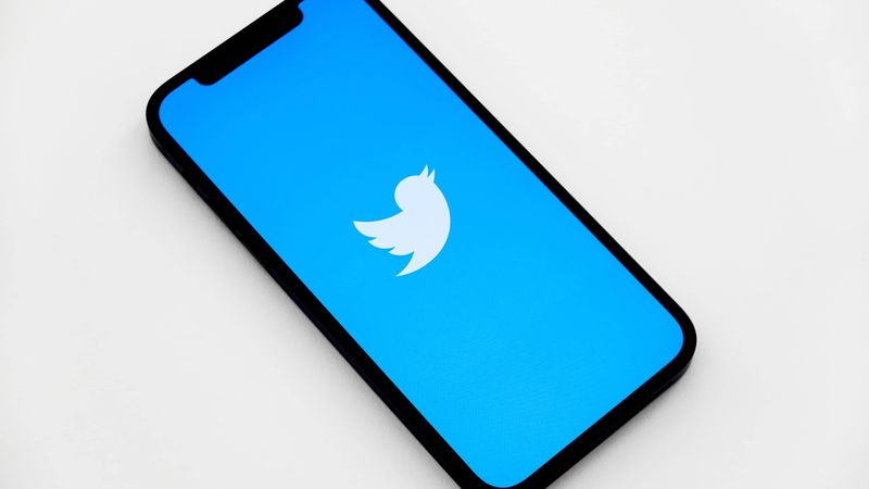 Isometric view of an iPhone showing a white Twitter bird logo on the screen, set against a sold light-blue background