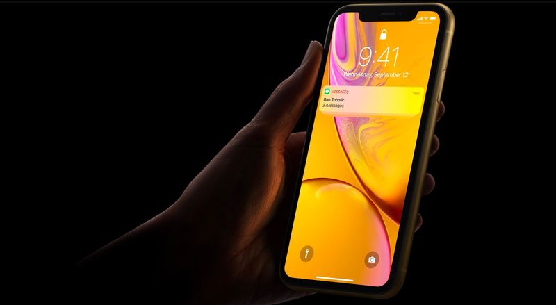 An image showing an iPhone XR held in hand, set against a dark background, with a Messages notification shown on the lock screen