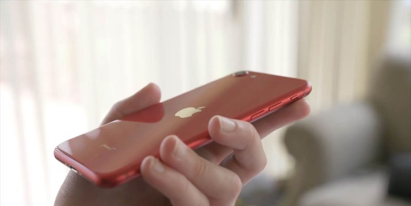 A photo showing a hand holding a red iPhone SE 2