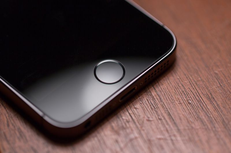 A photograph showing an iPhone laid flat on a table with a focus on the Touch ID button