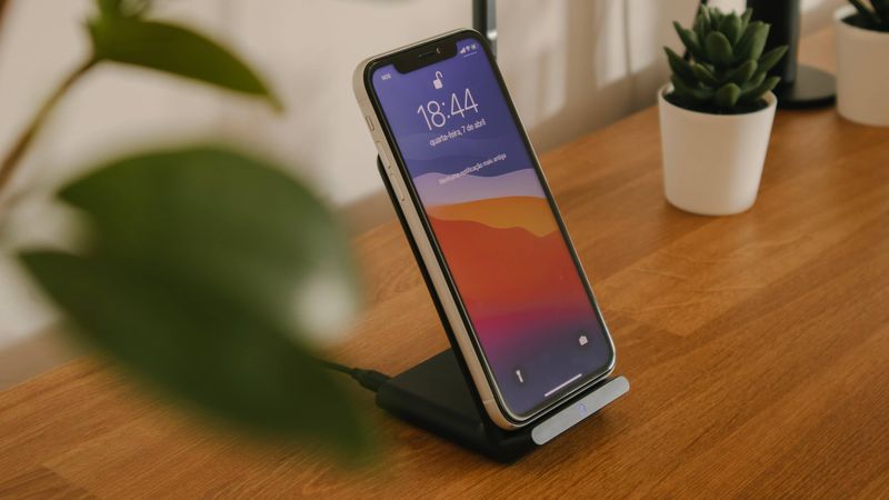 iPhone 13 sitting on a wireless charger set on a wooden desk