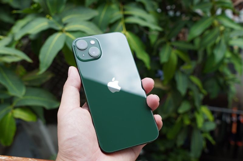 Tenir un iPhone 13 vert devant des buissons verts