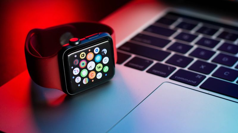 A black Apple Watch Series 7 is shown resting on its side next to the trackpad on Apple