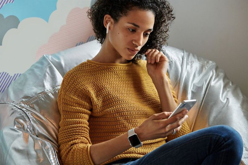 A person sitting on a couch, using her iPhone while listening to music on her AirPods. One leaker claims the next AirPods are launching at Apple
