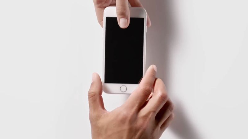  scene from Ap-in ad showing a male hand handing an iPhone 5s over to another male